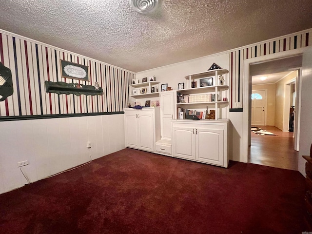 empty room with wallpapered walls, a wainscoted wall, dark carpet, and a textured ceiling