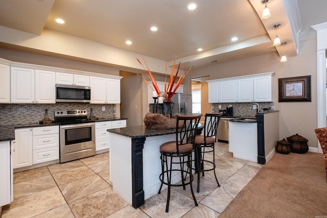 kitchen with a breakfast bar area, white cabinets, a kitchen island, backsplash, and appliances with stainless steel finishes