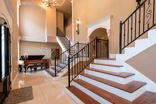 stairs featuring a notable chandelier, a towering ceiling, and tile patterned floors