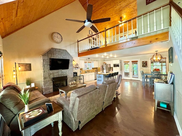 living room featuring dark hardwood / wood-style floors, ceiling fan with notable chandelier, a stone fireplace, wood ceiling, and high vaulted ceiling