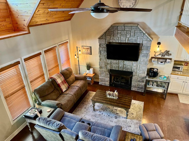 living room with ceiling fan, dark hardwood / wood-style floors, a stone fireplace, and high vaulted ceiling