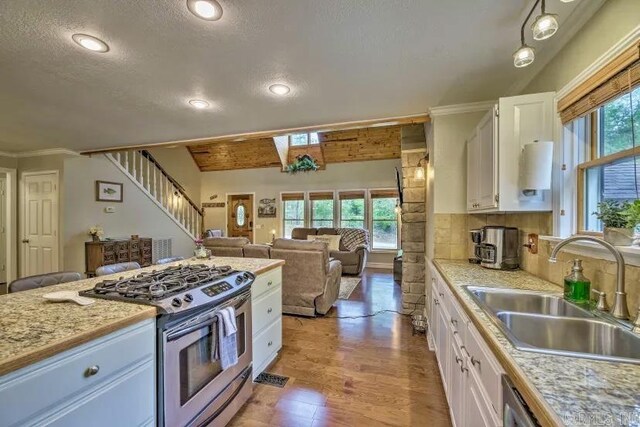 kitchen with a sink, gas stove, white cabinets, light countertops, and decorative backsplash