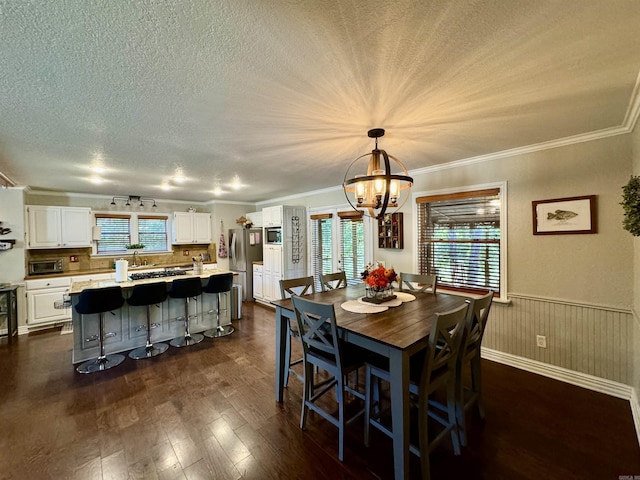 dining space with a notable chandelier, ornamental molding, a textured ceiling, dark wood finished floors, and wainscoting