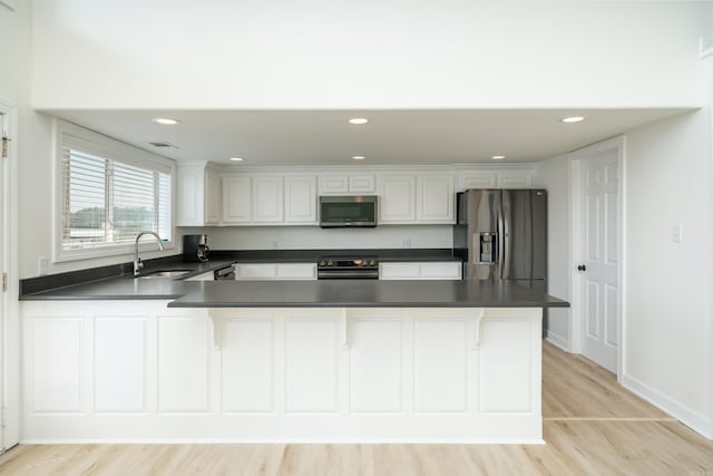 kitchen with appliances with stainless steel finishes, kitchen peninsula, sink, white cabinetry, and light wood-type flooring