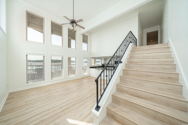 stairway with ceiling fan, hardwood / wood-style flooring, and a towering ceiling