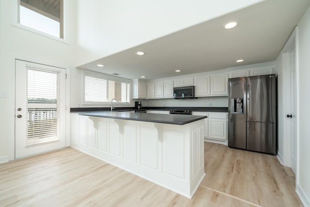 kitchen featuring a kitchen breakfast bar, stainless steel appliances, kitchen peninsula, white cabinetry, and light wood-type flooring