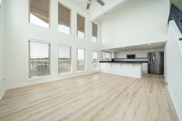 unfurnished living room with a healthy amount of sunlight, ceiling fan, high vaulted ceiling, and light hardwood / wood-style floors