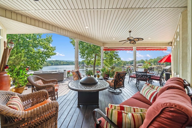 exterior space featuring a water view, ceiling fan, an outdoor living space with a fire pit, and a hot tub