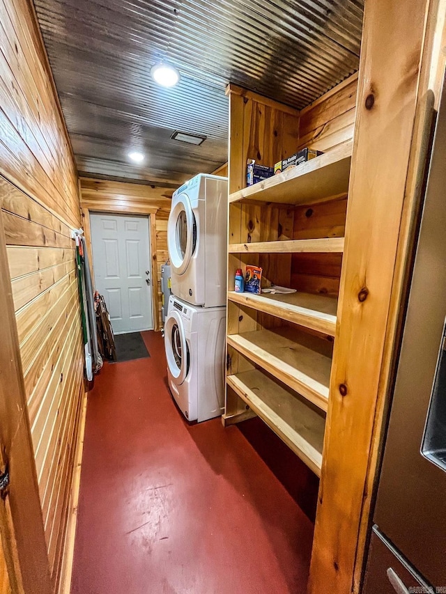 laundry area with wooden walls and stacked washer / drying machine