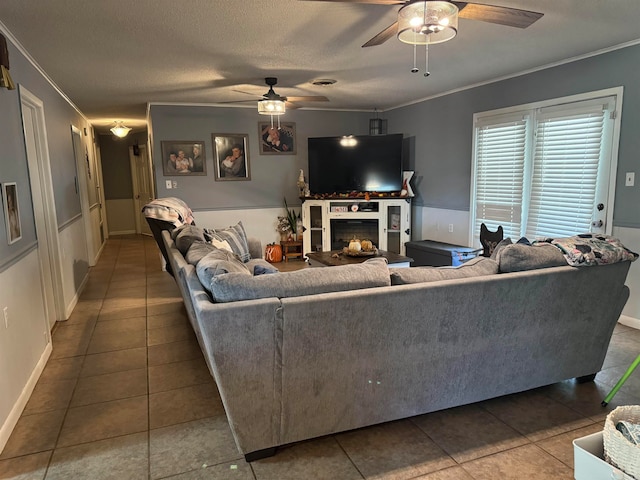 tiled living room featuring ceiling fan, a fireplace, a textured ceiling, and ornamental molding