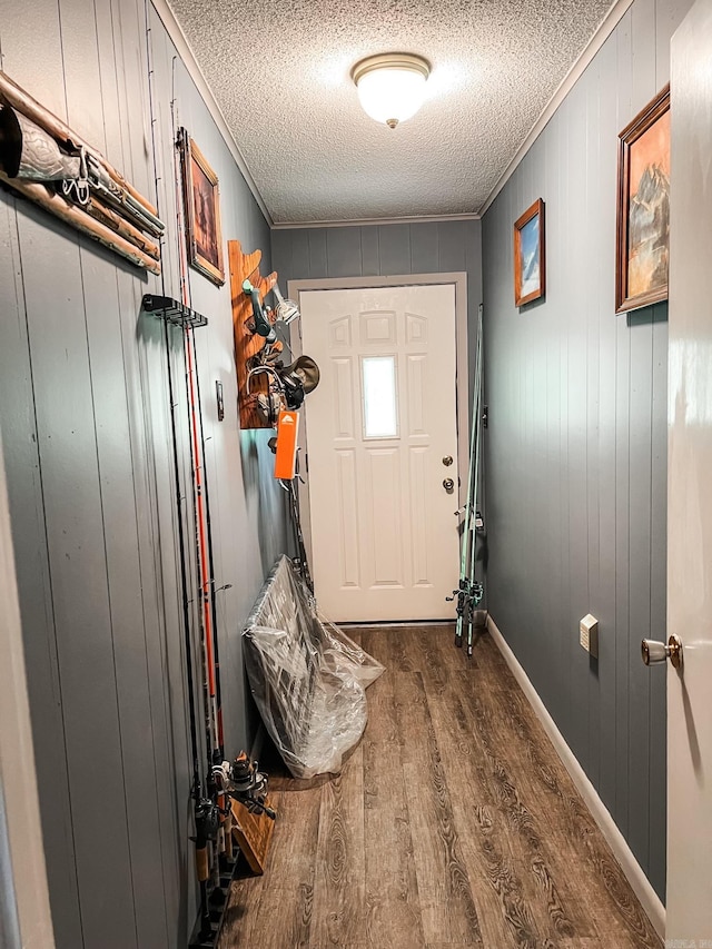 doorway with ornamental molding, dark wood-type flooring, a textured ceiling, and wooden walls