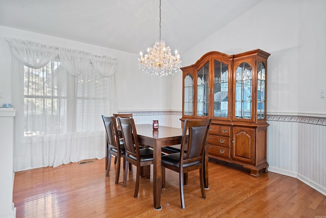 dining space featuring a wainscoted wall, a chandelier, light wood-style flooring, and vaulted ceiling