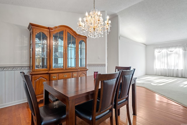 dining space featuring a chandelier, a wainscoted wall, a textured ceiling, and wood finished floors