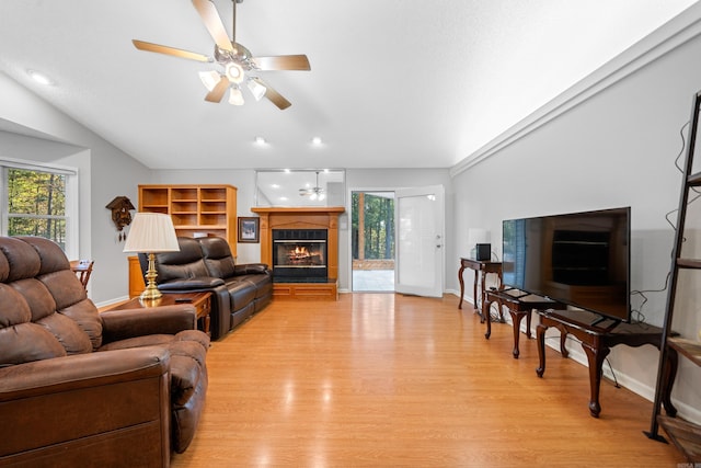 living area featuring a ceiling fan, a glass covered fireplace, vaulted ceiling, and light wood finished floors