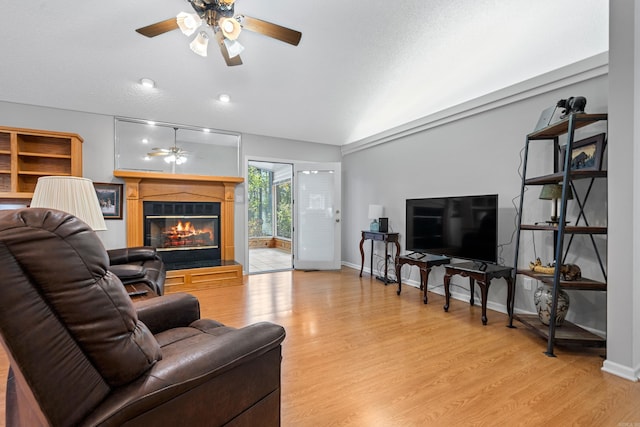 living room with baseboards, wood finished floors, a glass covered fireplace, and a ceiling fan