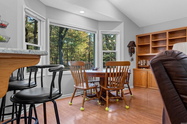 dining room featuring light wood-style flooring, baseboards, and vaulted ceiling