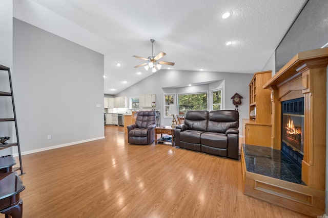 living room with ceiling fan, baseboards, light wood-type flooring, lofted ceiling, and a glass covered fireplace