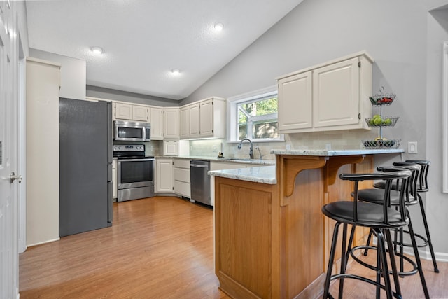 kitchen featuring light stone counters, a peninsula, light wood-style floors, stainless steel appliances, and a sink