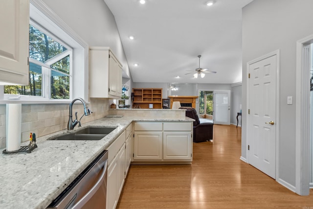 kitchen featuring light stone counters, a peninsula, a sink, dishwasher, and light wood-type flooring