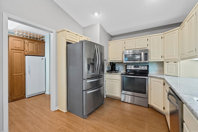 kitchen with backsplash, light wood-type flooring, light stone counters, stainless steel appliances, and a textured ceiling