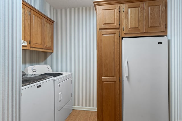 washroom featuring wallpapered walls, baseboards, washing machine and dryer, light wood-style floors, and cabinet space