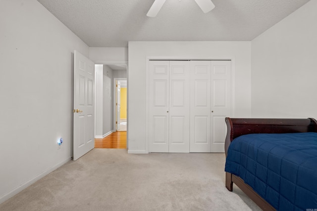 bedroom with baseboards, ceiling fan, light colored carpet, a closet, and a textured ceiling