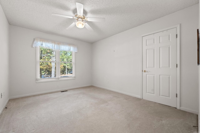 carpeted empty room featuring a textured ceiling, visible vents, baseboards, and ceiling fan