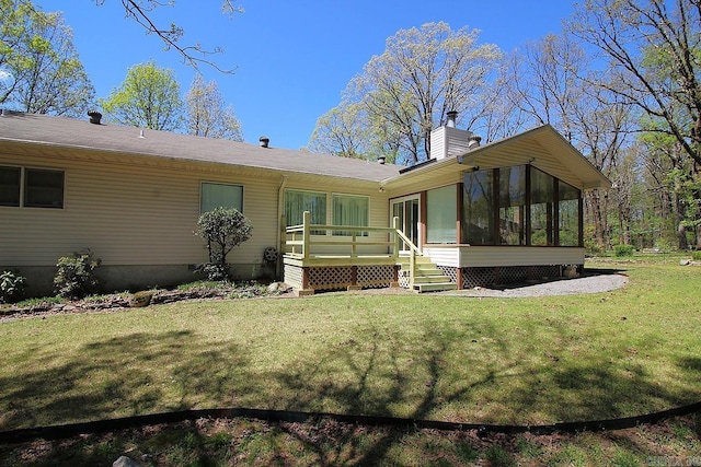 rear view of house with a lawn, a chimney, a sunroom, and a wooden deck
