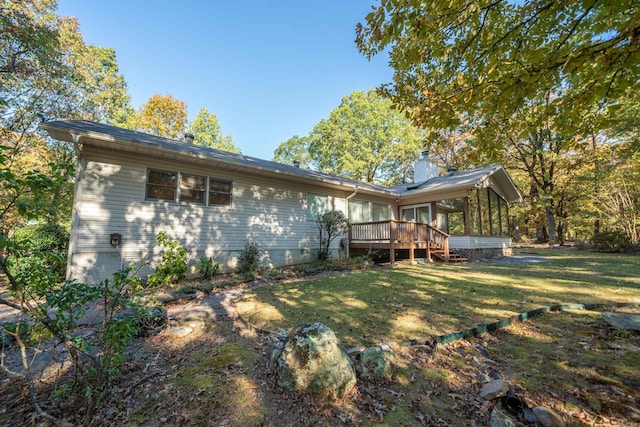 rear view of house with a wooden deck, a yard, a sunroom, and a chimney