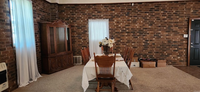 carpeted dining space with heating unit, visible vents, and brick wall