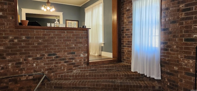 interior space featuring an inviting chandelier, brick wall, and ornamental molding