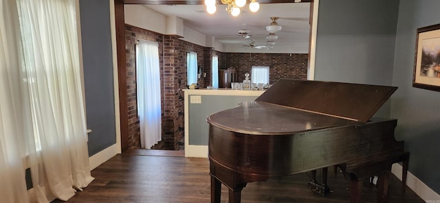 interior space featuring wood finished floors, ceiling fan with notable chandelier, and brick wall