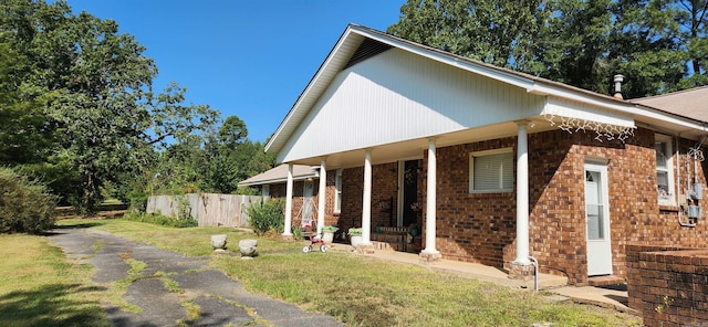 view of side of property with brick siding, aphalt driveway, a lawn, and fence