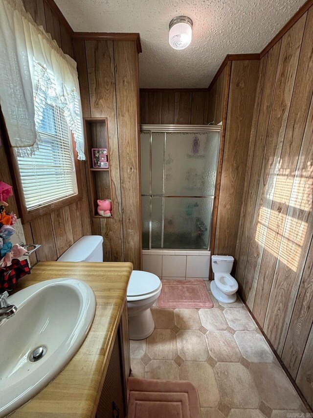 full bathroom featuring bath / shower combo with glass door, wood walls, toilet, vanity, and a textured ceiling