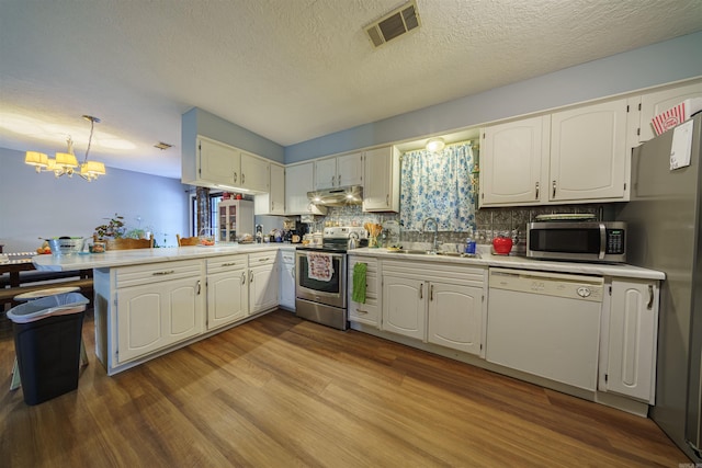 kitchen with hardwood / wood-style flooring, stainless steel appliances, a chandelier, sink, and kitchen peninsula