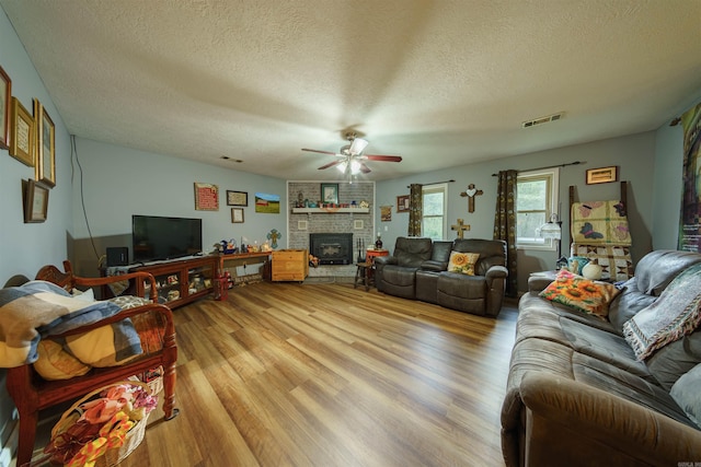 living room with light wood-type flooring, ceiling fan, a textured ceiling, and a brick fireplace