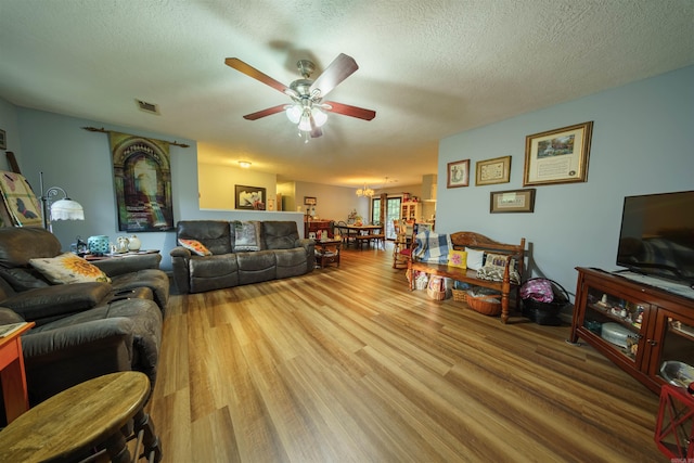 living room featuring light wood-type flooring, ceiling fan, and a textured ceiling