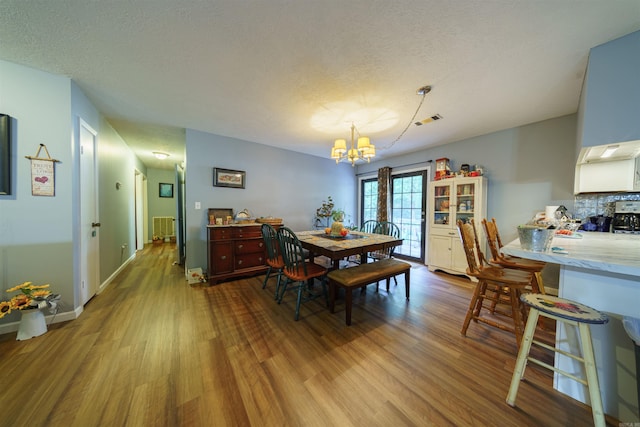 dining area with radiator, light hardwood / wood-style floors, a notable chandelier, and a textured ceiling