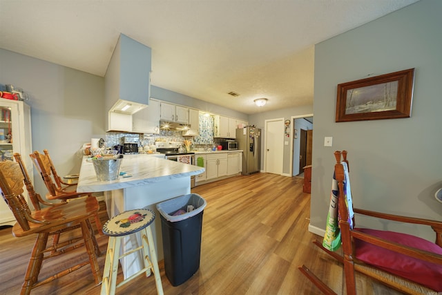 kitchen featuring appliances with stainless steel finishes, light hardwood / wood-style floors, white cabinetry, kitchen peninsula, and a kitchen bar