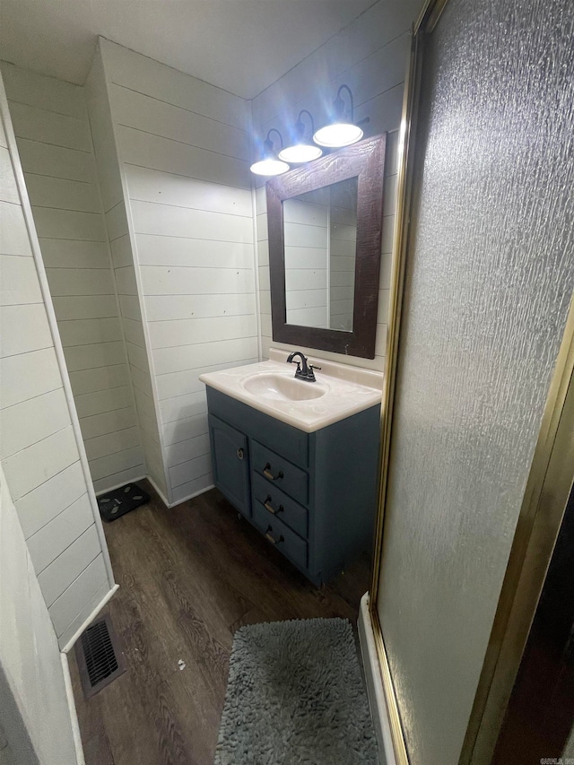 bathroom featuring vanity, wood-type flooring, a shower with door, and wood walls