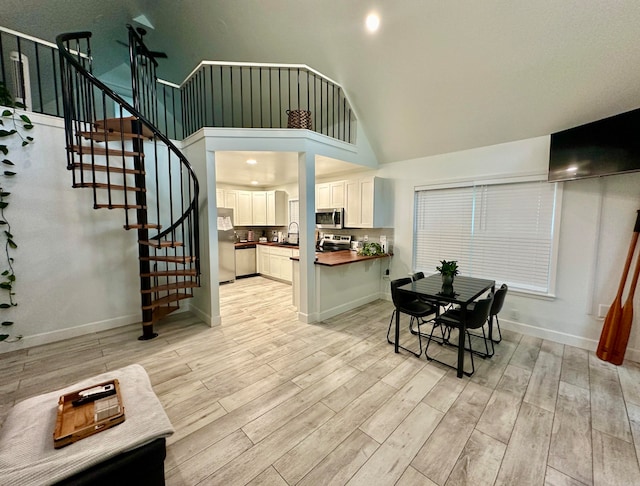 dining space featuring light hardwood / wood-style floors, high vaulted ceiling, and sink