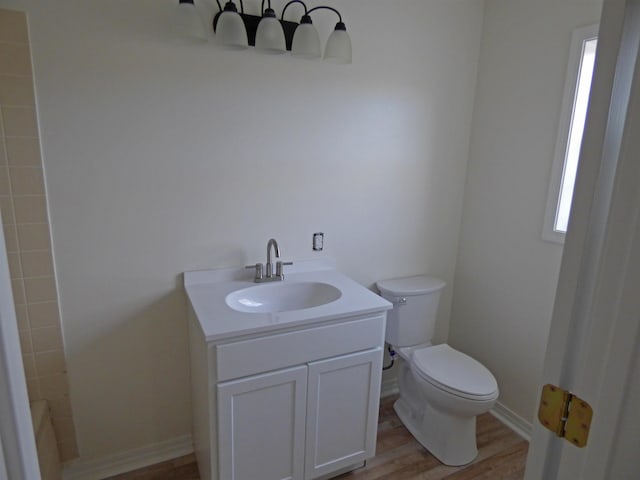 bathroom featuring baseboards, toilet, wood finished floors, vanity, and a shower