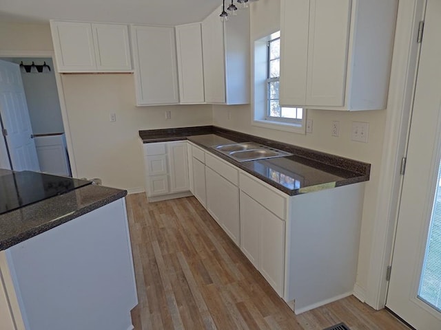 kitchen with light wood finished floors, dark stone countertops, white cabinets, and a sink