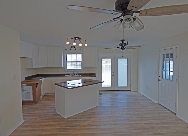 kitchen with dark countertops, light wood-style flooring, french doors, white cabinetry, and a sink