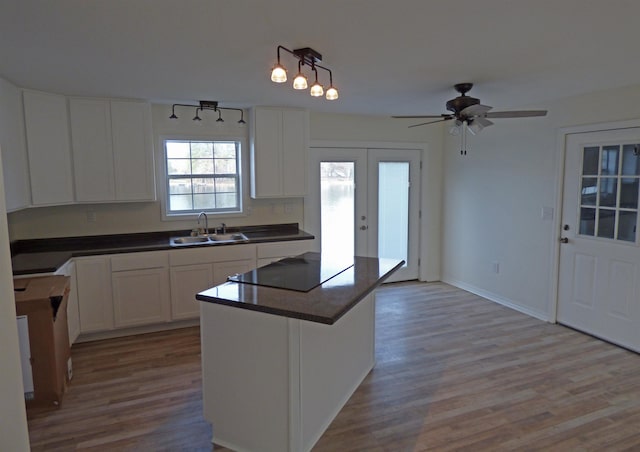 kitchen with a sink, black electric cooktop, light wood-style floors, and dark countertops