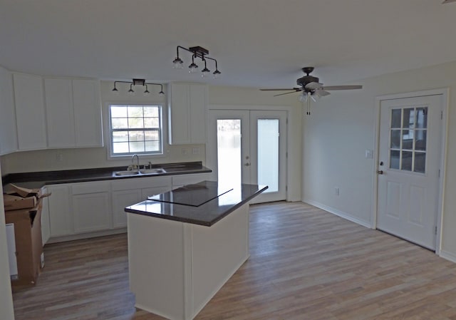 kitchen with a sink, black electric cooktop, light wood-type flooring, and dark countertops