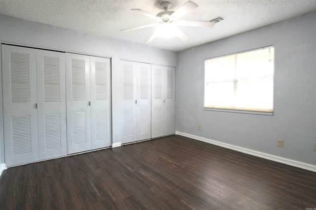 unfurnished bedroom featuring multiple closets, a textured ceiling, ceiling fan, and dark hardwood / wood-style floors