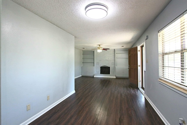 unfurnished living room with dark wood-type flooring, ceiling fan, a textured ceiling, and a brick fireplace