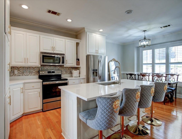 kitchen with a notable chandelier, appliances with stainless steel finishes, light hardwood / wood-style floors, an island with sink, and sink