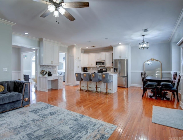 living room featuring ceiling fan with notable chandelier, ornamental molding, and light hardwood / wood-style flooring